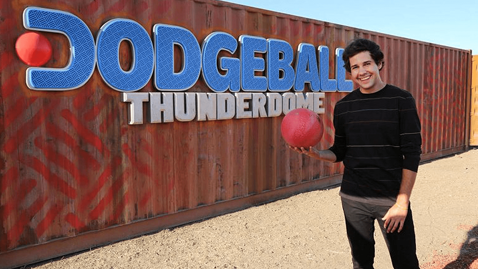 David Dobrik stands next to a metal shipping container with the words "Dodgeball: Thunderdome"