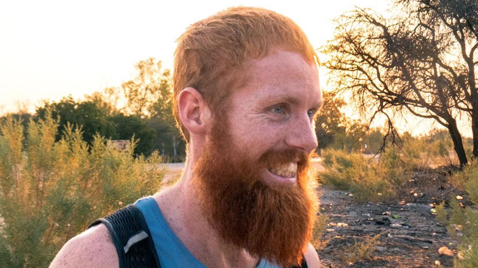 The Hardest Geezer stood on dirt path wearing blue tank top