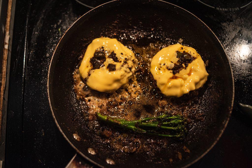 Two burgers cooking in a frying pan.