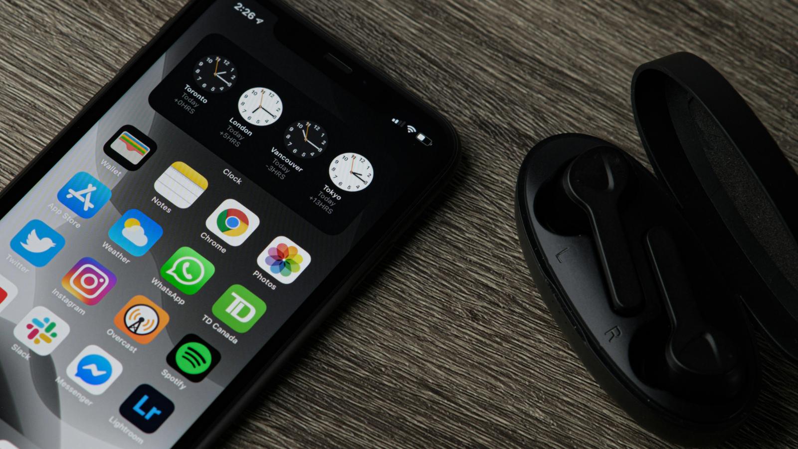 An iPhone placed in a wooden table next to earphones