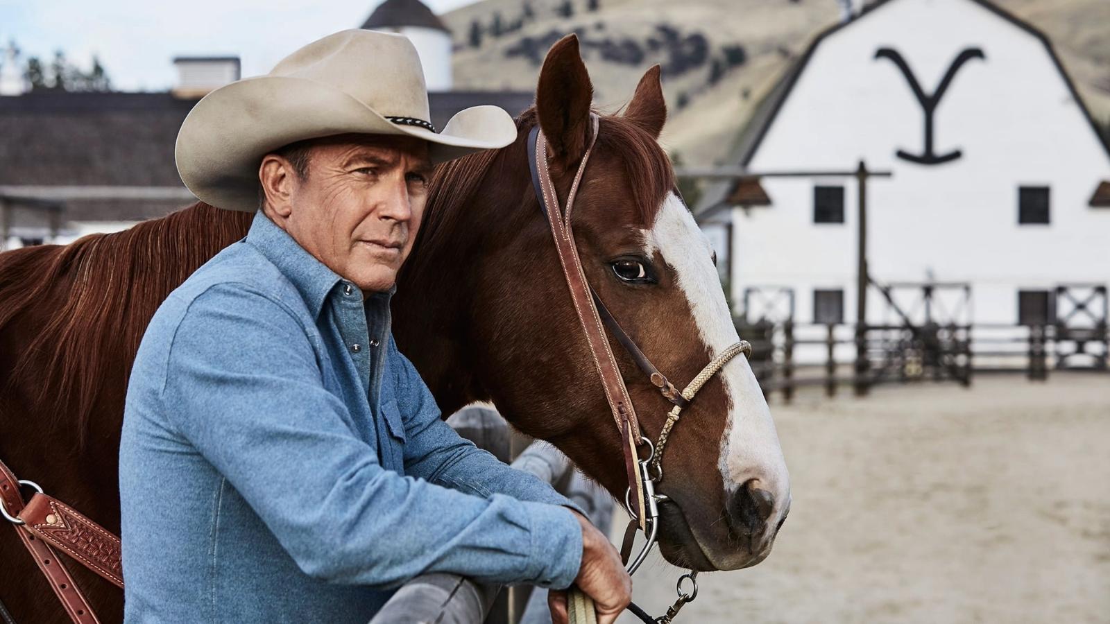 Kevin Costner as John Dutton, standing with his horse outside a barn on the Dutton Ranch