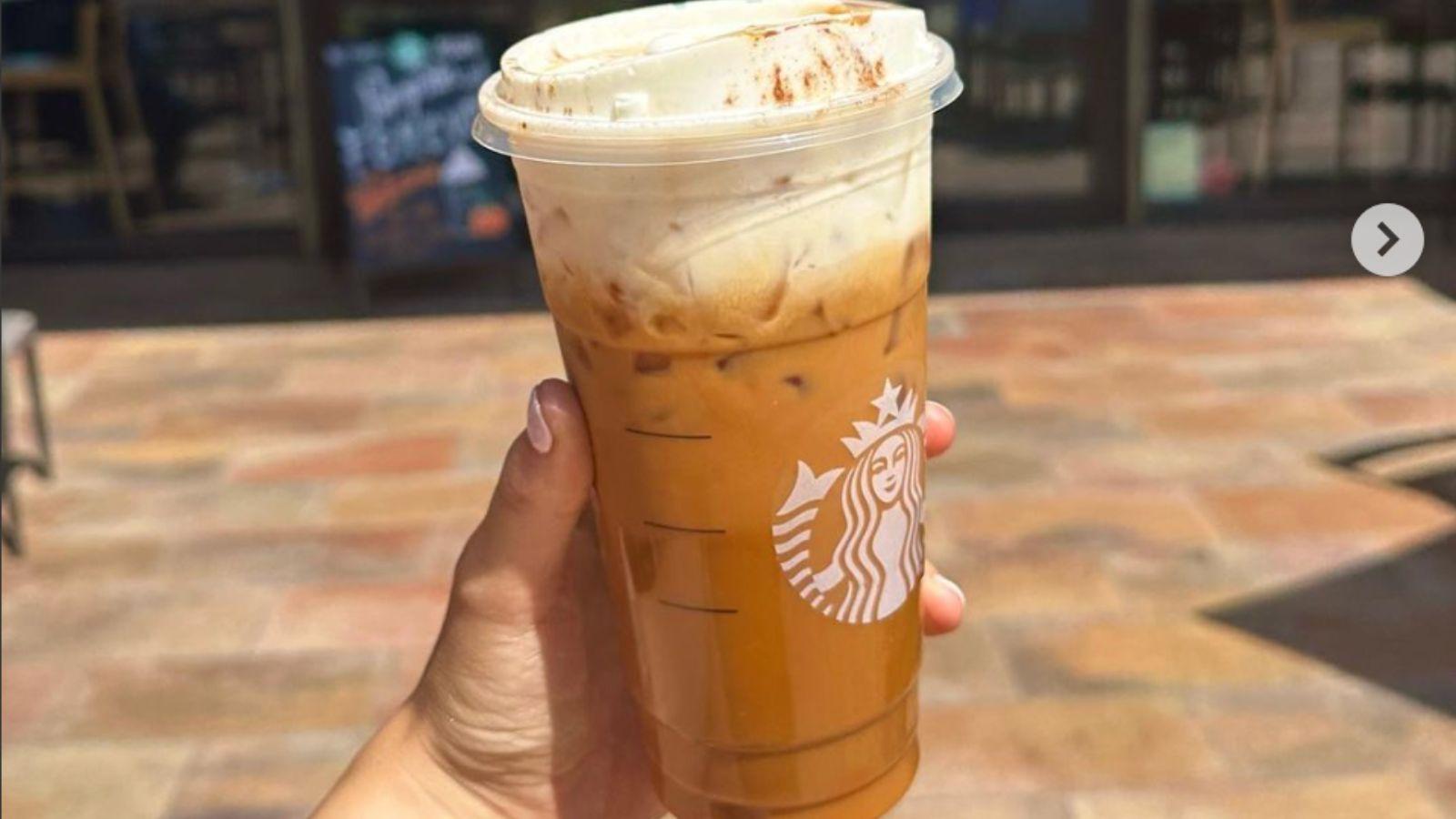 A hand holding a big Starbucks cup filled with iced pumpkin spiced latte