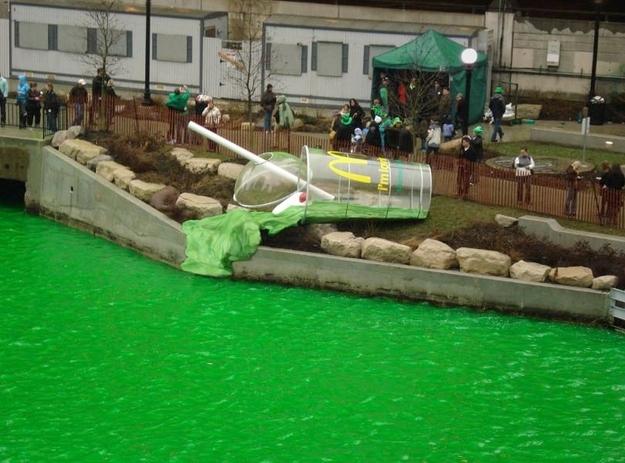 A giant shamrock shake sculpture spilling into a river dyed green.