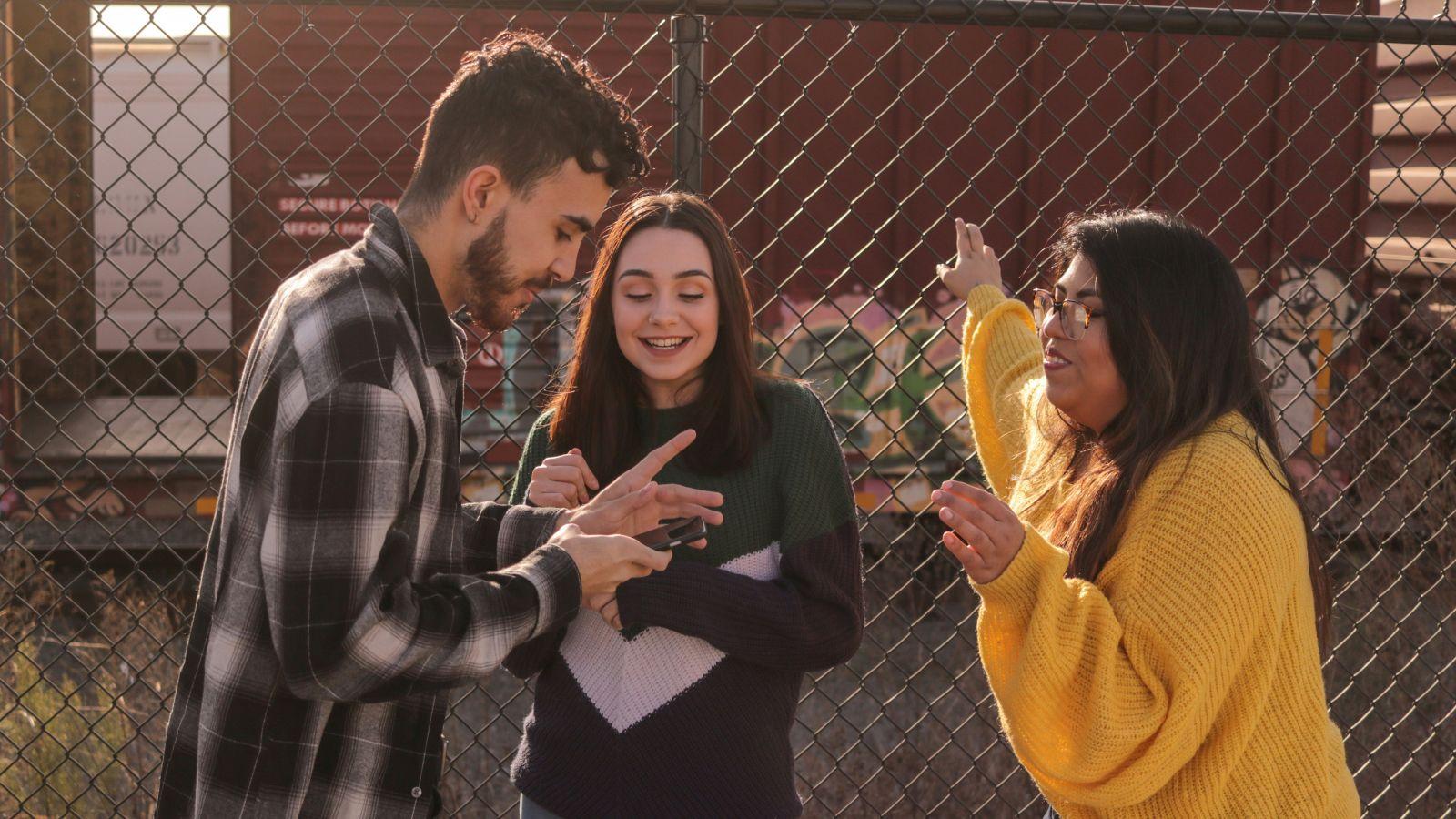 A man and two women looking at a phone while laughing