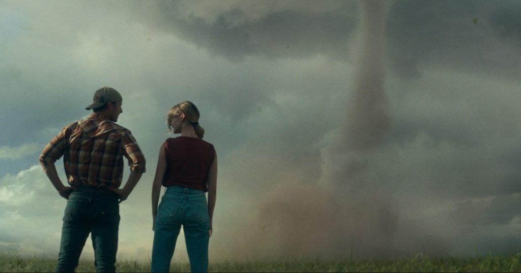 Glen Powell and Daisy Edgar-Jones as Tyler and Kate, standing in a field and staring at a twister in Twisters