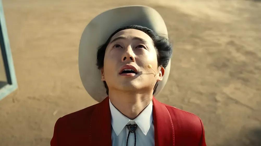 Steven Yeun as Ricky "Jupe" Park, looking up at the sky with his cowboy hat being blown off