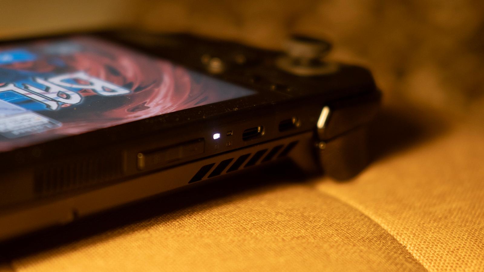 Asus ROG Ally X displaying Balatro, but the camera is focused on the two usb-c ports on the top, on a yellow cushion surface